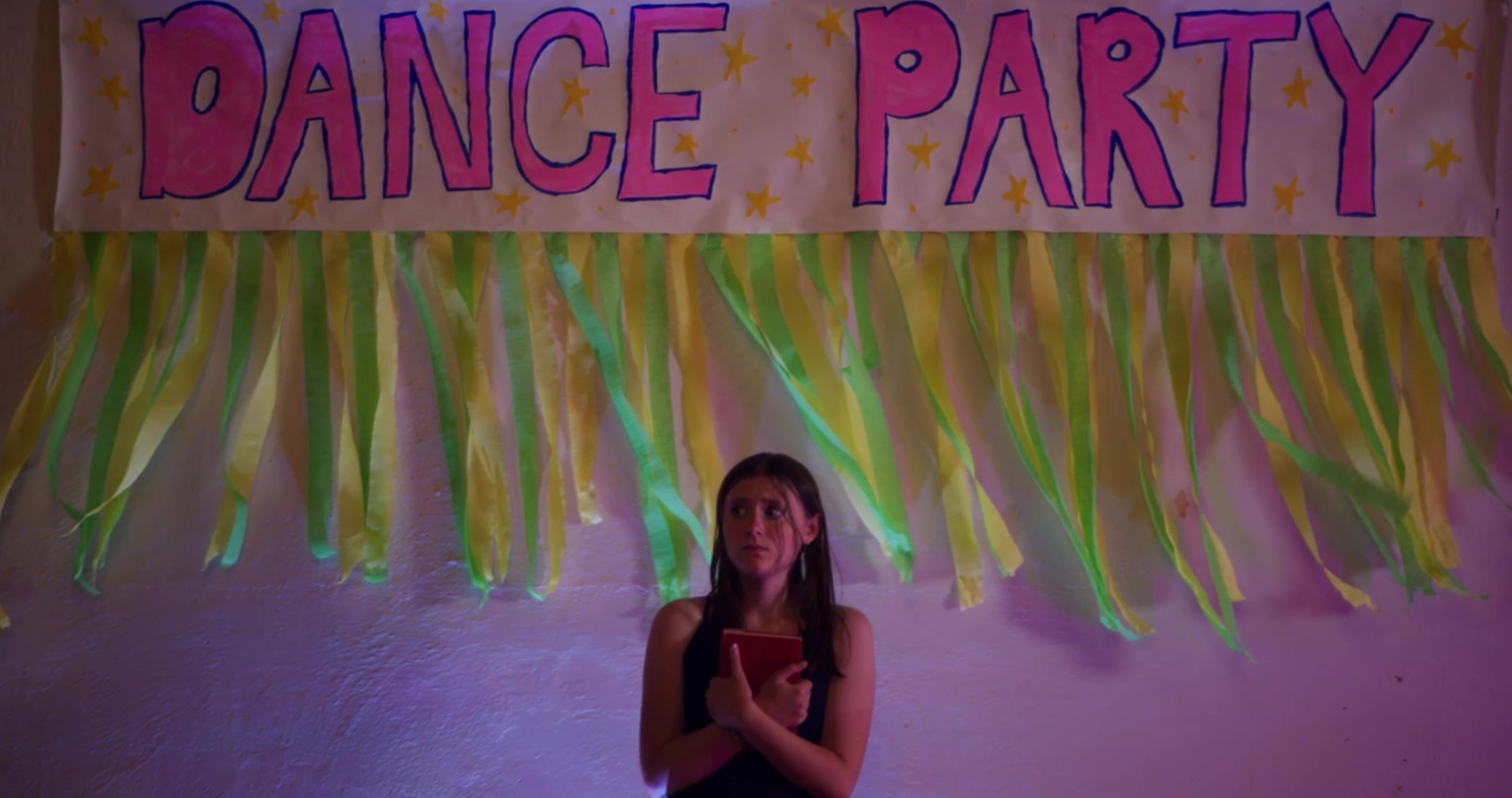 Olivia clutches her book under a hand-painted Dance Party banner.