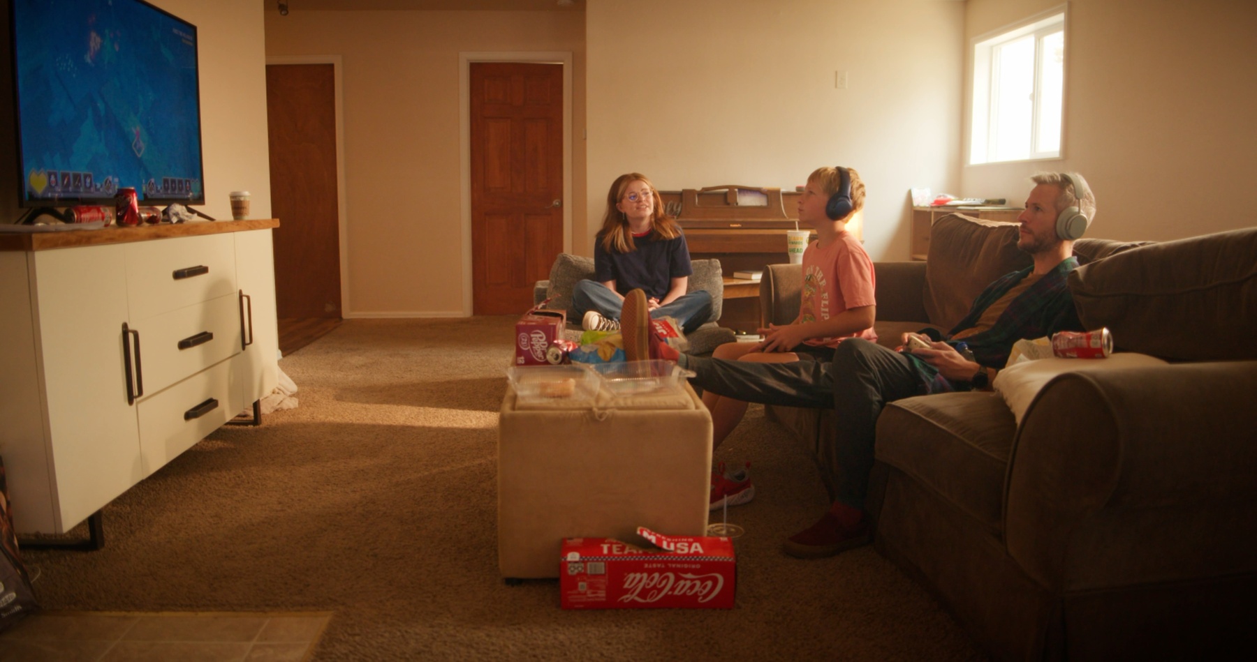 A family sits together on the couch, headphones on, watching a game.