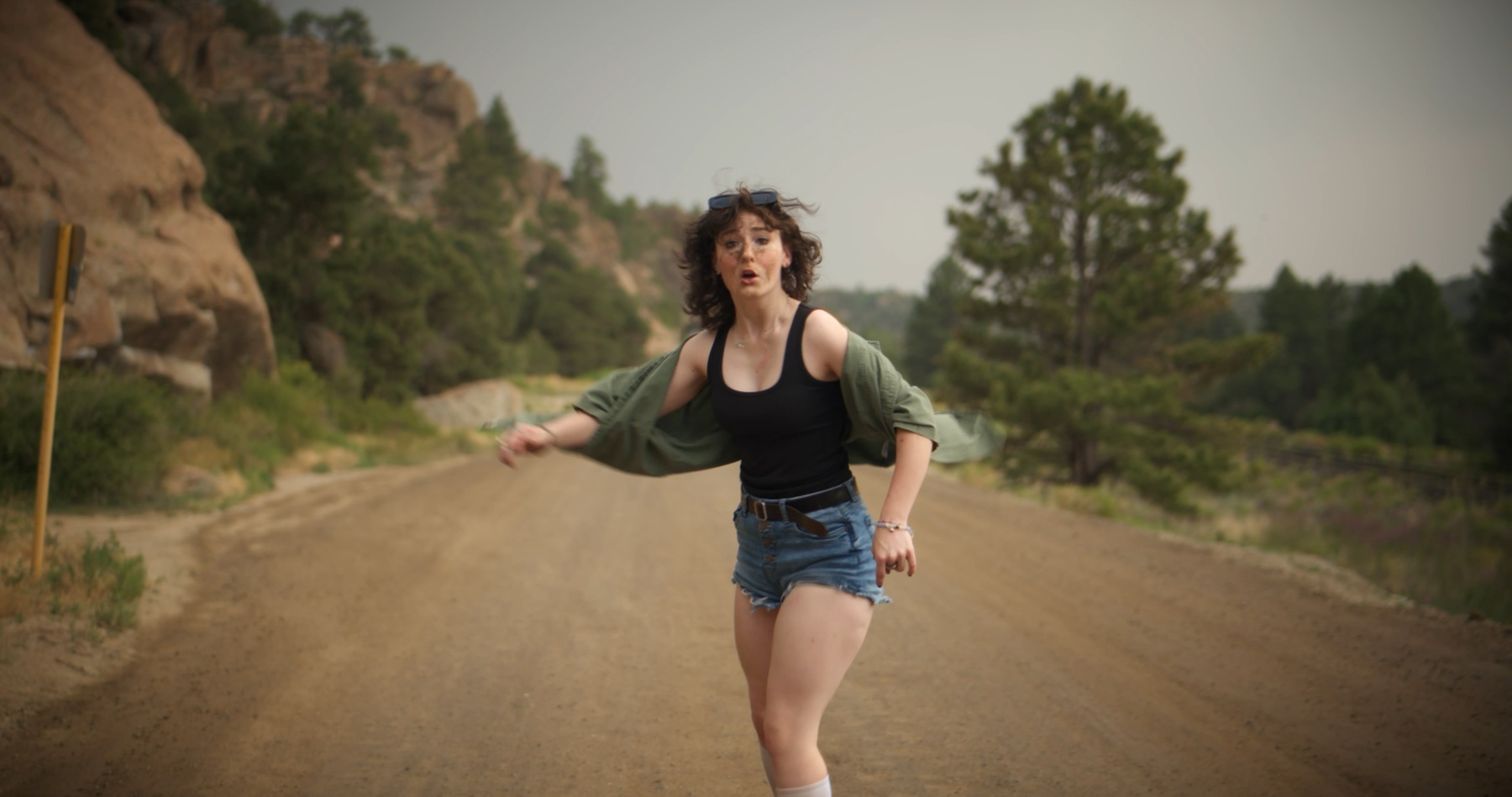 Olivia stumbles down a dirt mountain road, wind-blown and startled.