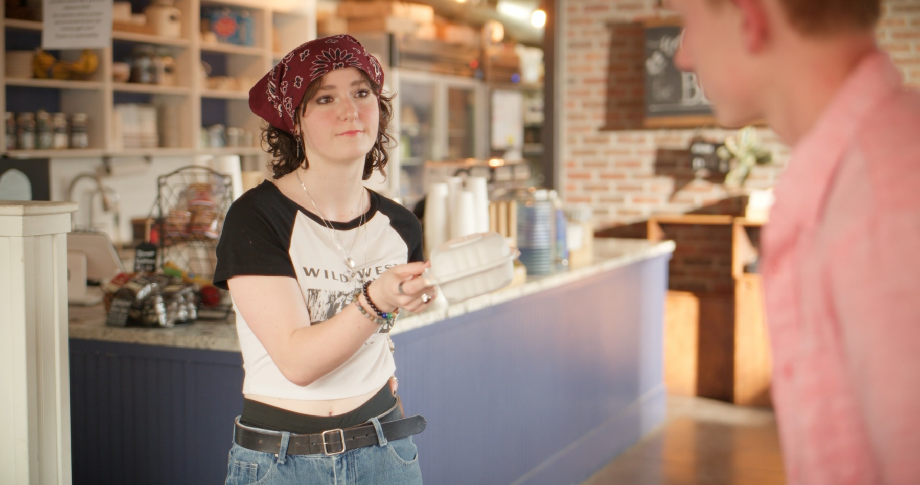 Maddy hands over a to-go order, wearing a Wild West t-shirt.