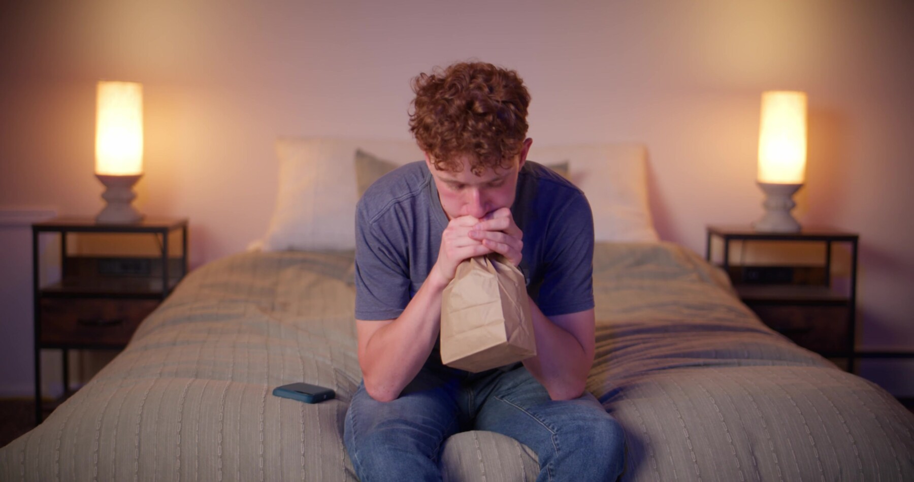 Ryan sits on his bed, breathing into a paper bag.