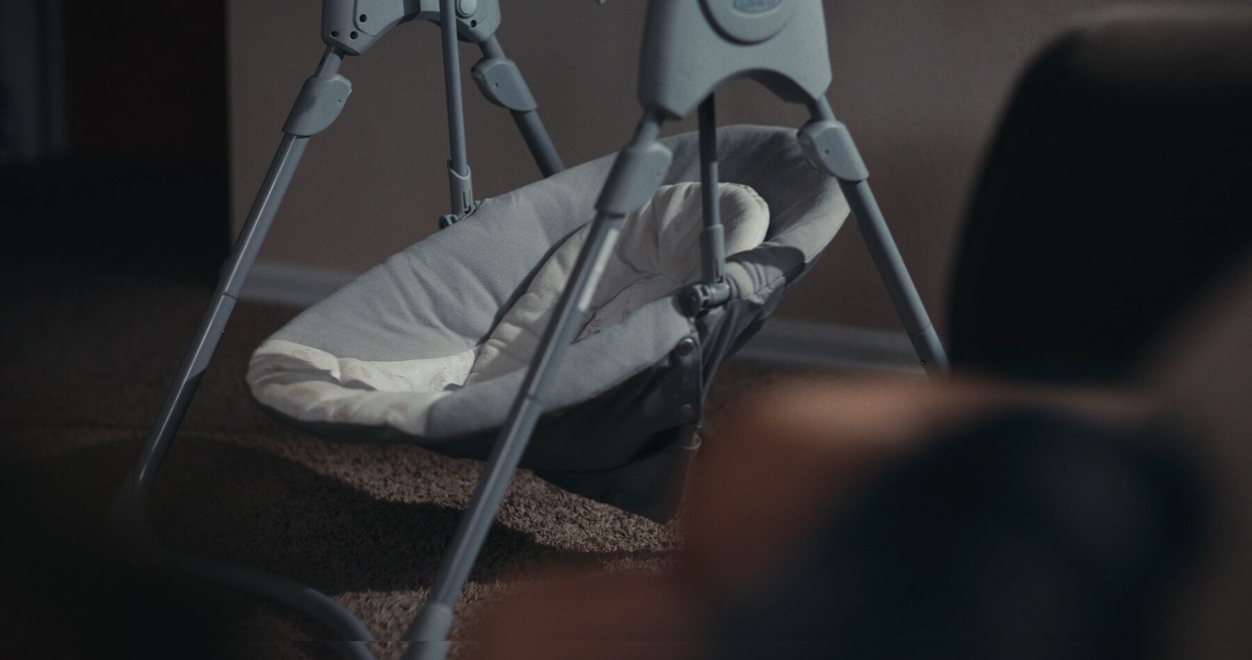 An empty baby swing sits in a dim room.