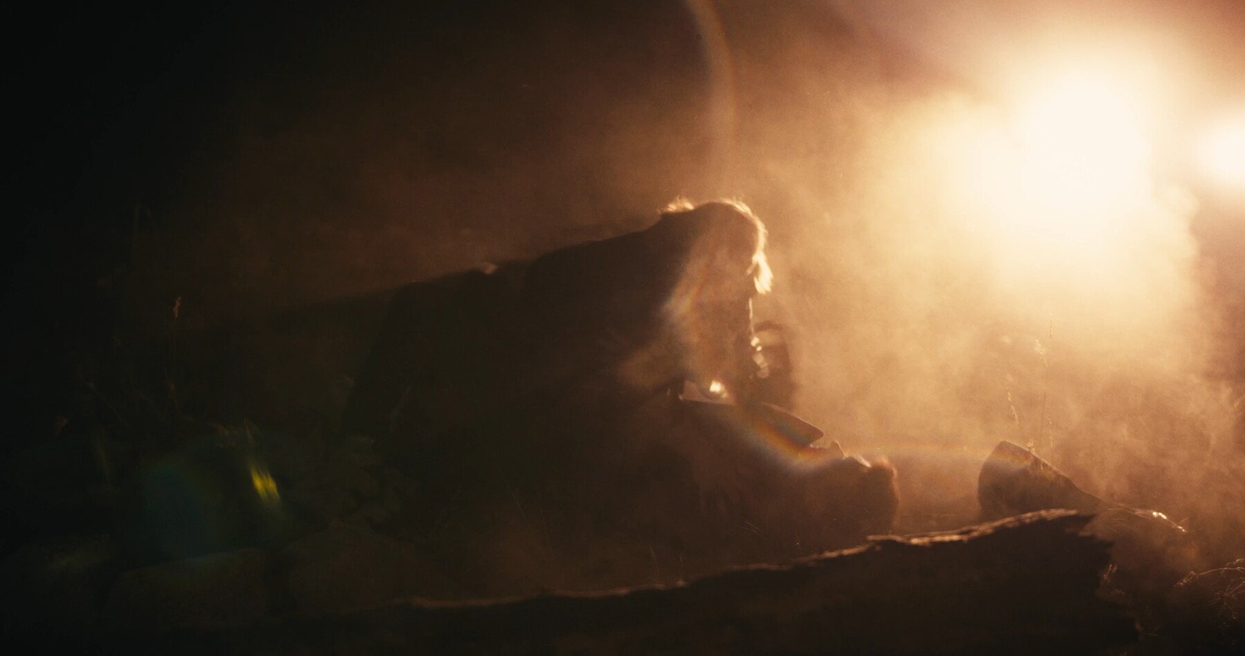A figure lies in silhouette against a bright backlight at night.