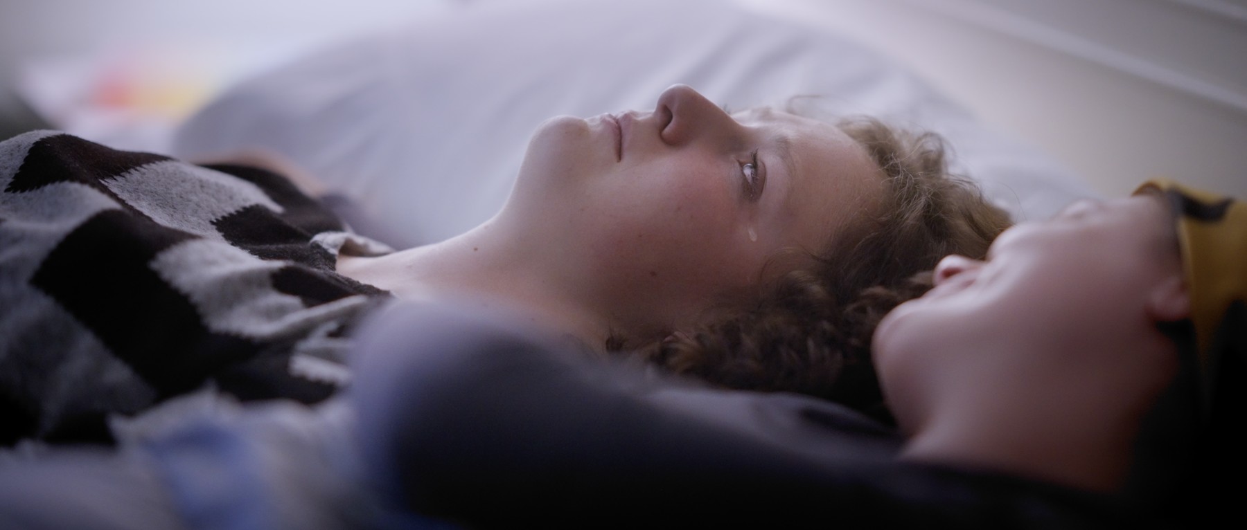 Two young women lie side by side, one looking toward the other.
